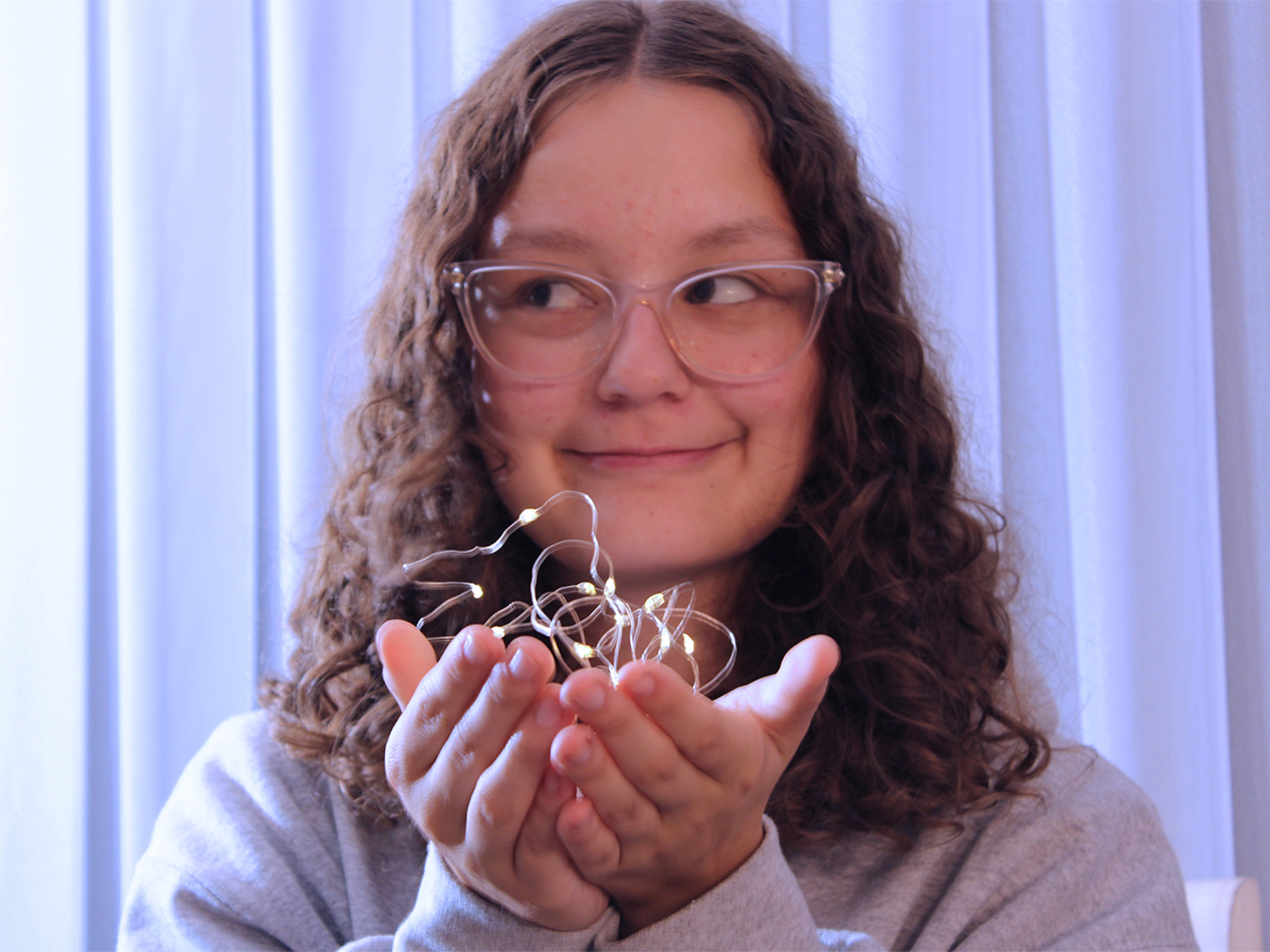 teen girl with glasses smiling and looking at fairy lights she is holding in her hands