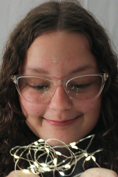 teen girl with glasses smiling and looking at fairy lights she is holding in her hands