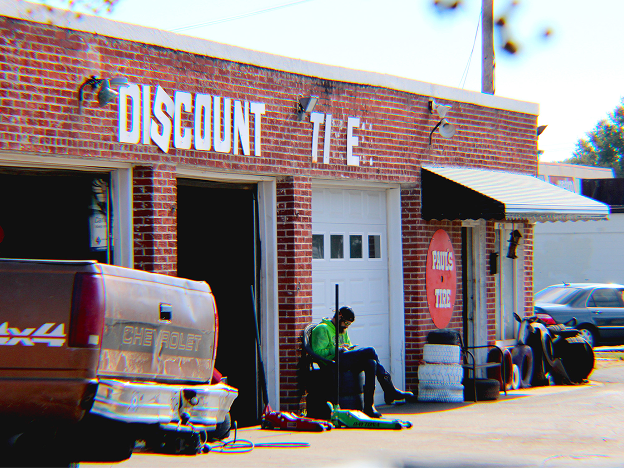 man sitting outside in front of old brick building that's a discount tire shop