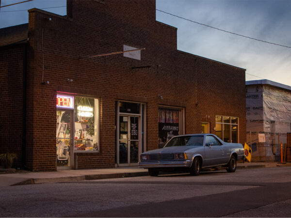 el camino parked on street at sunset in front of brick building with neon open sign in window