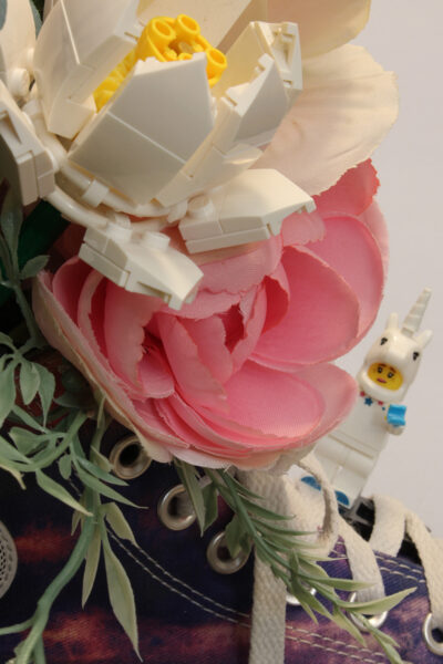 lego unicorn hanging onto high top converse that is being used as vase with flowers