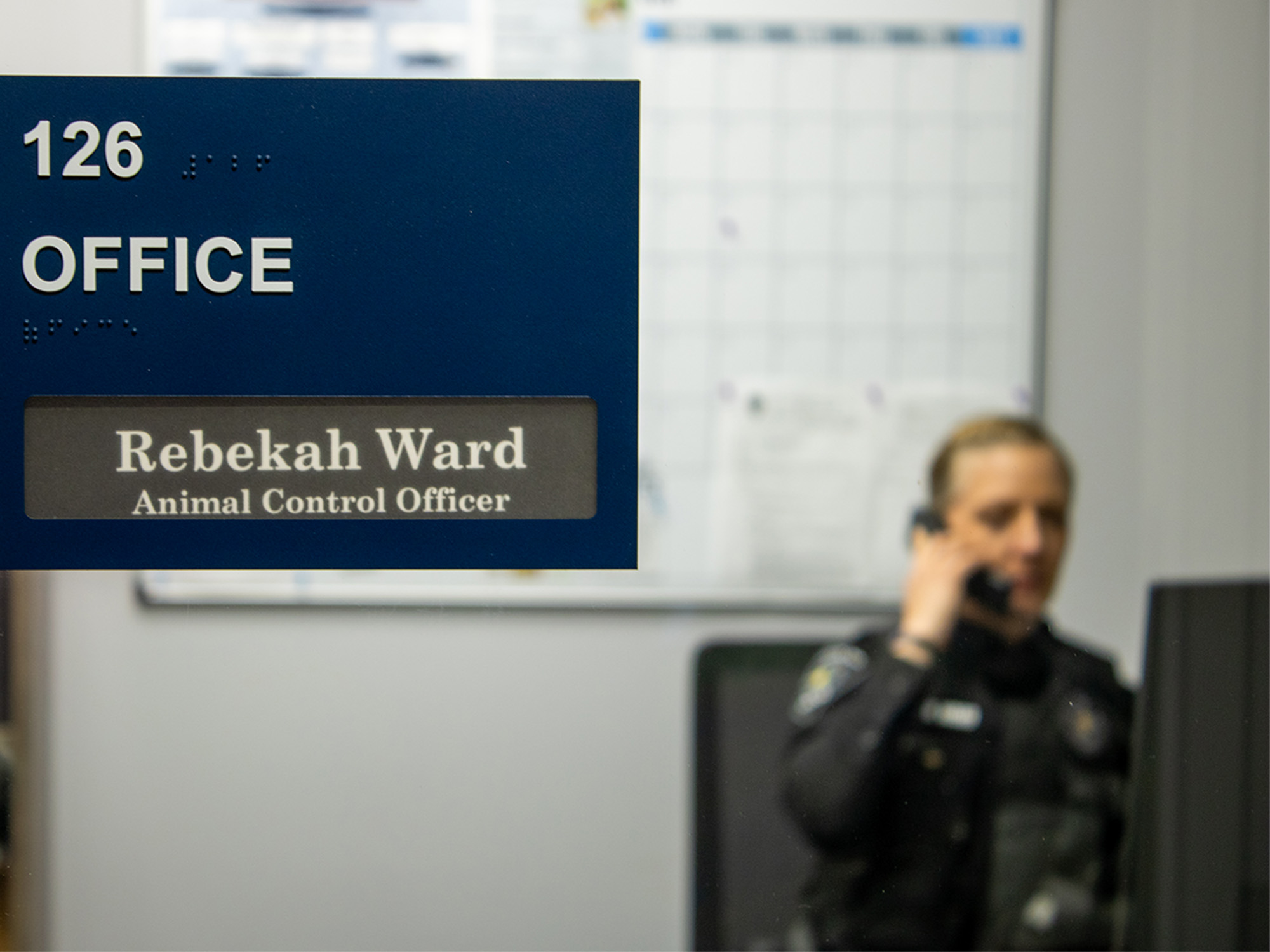 officer plaque on window with officer in background at desk on phone