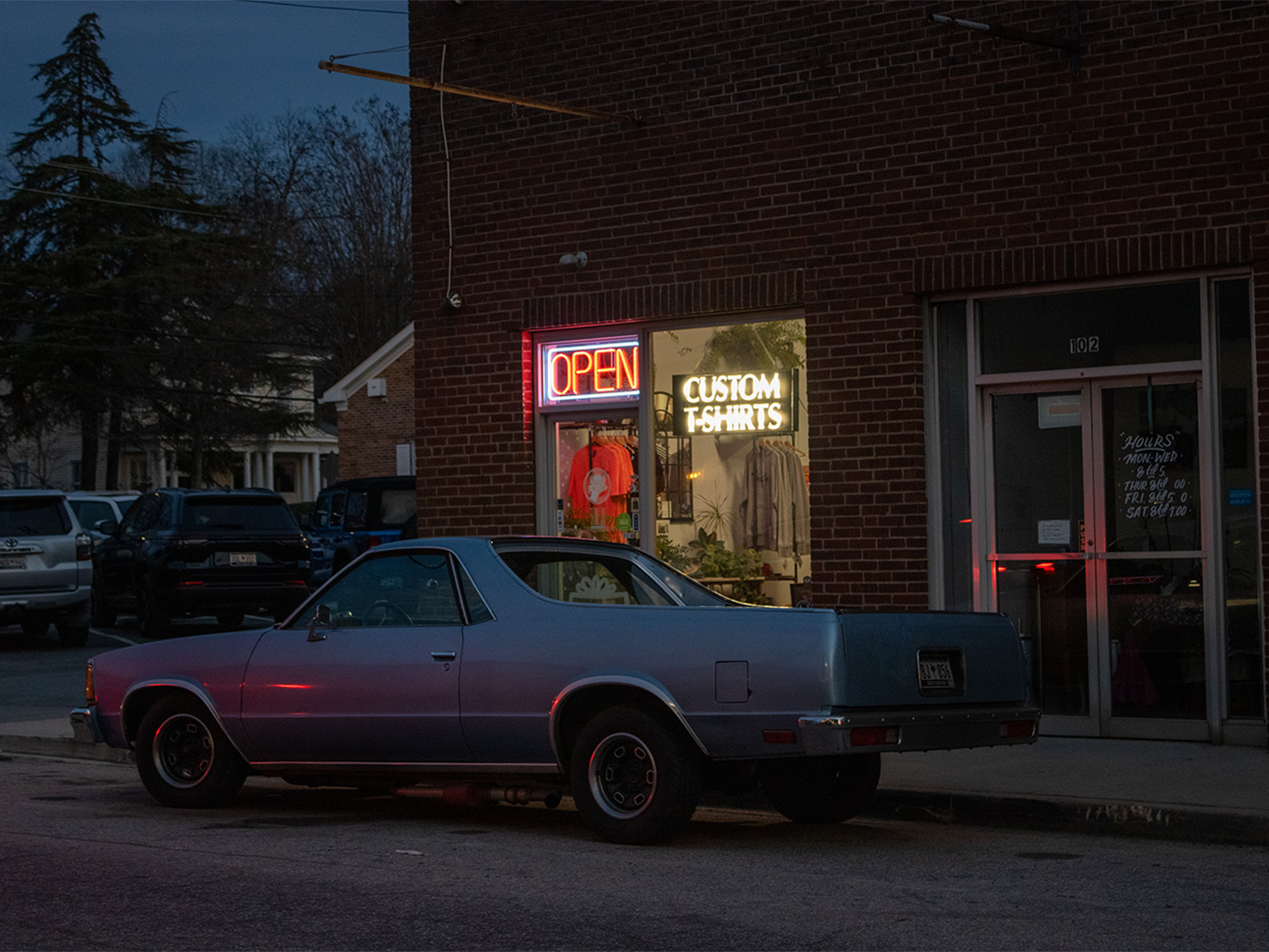 el camino parked in front of a brick building with neon open sign in window
